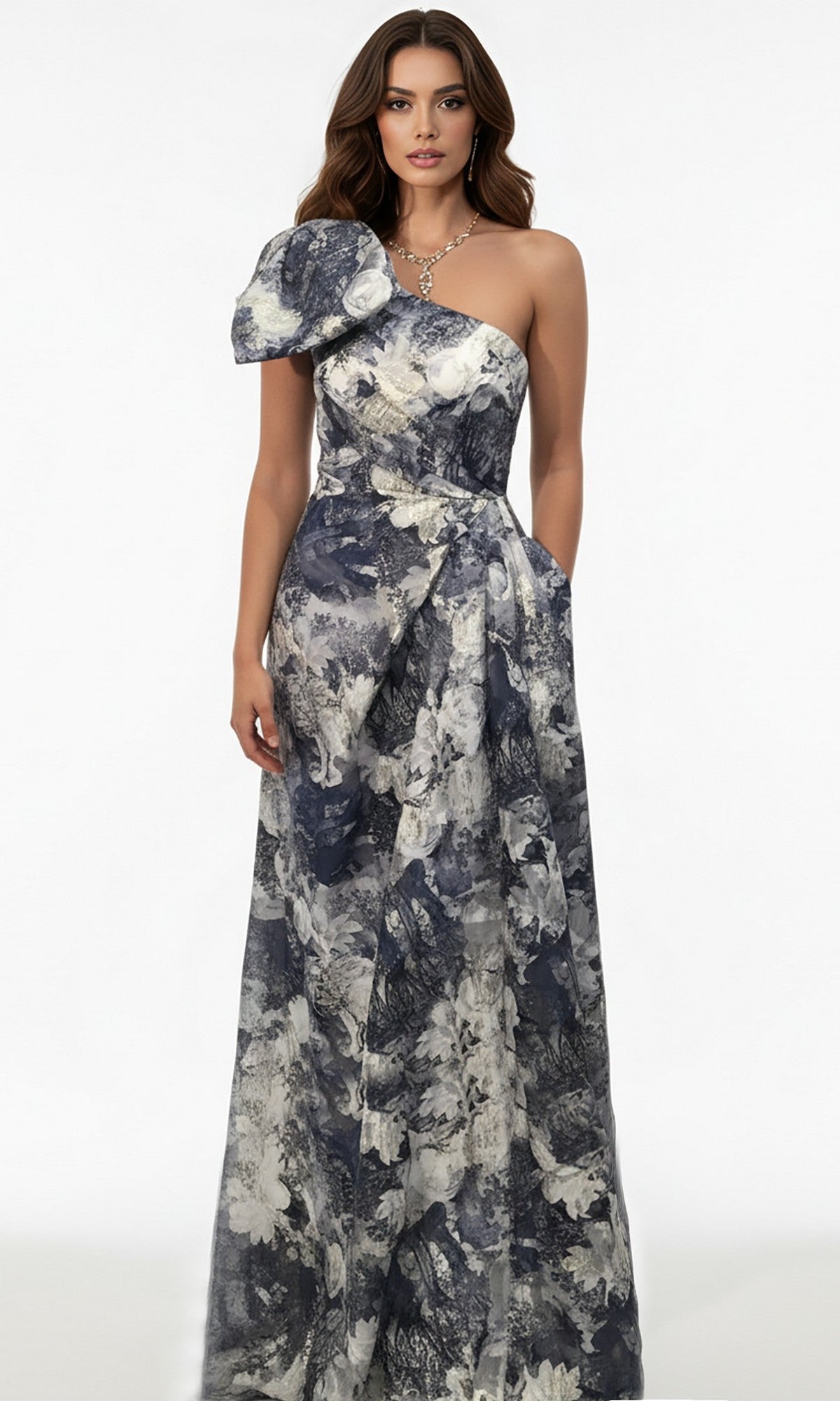 A woman stands against a white background wearing the Jovani 25663 long formal dress, which features an A-line skirt, one-shoulder design with a bold shoulder detail, and a grey and white floral pattern.